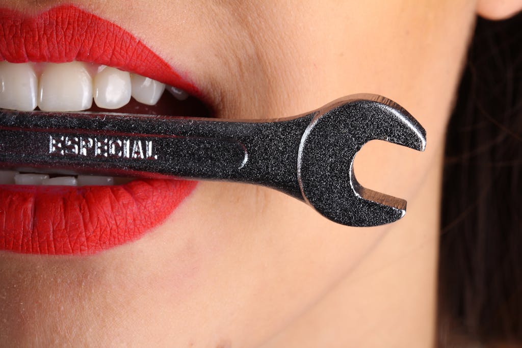 A close-up shot of red lips holding a shiny wrench with bold red lipstick.